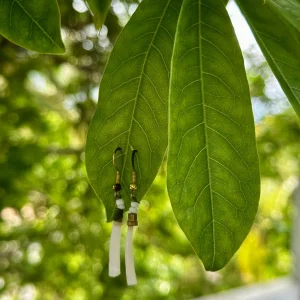 Natural dentalium shell earrings hanging on a green leaf, featuring tusk shells for handmade jewelry, beadwork, and eco-friendly shell accessories.